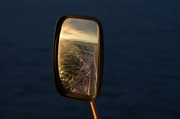 Side mirror of a boat reflecting the ocean and wake at dusk