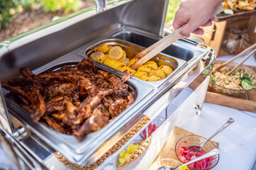 hand of a man picking up grilled ribs with corn and dip in heating steel box
