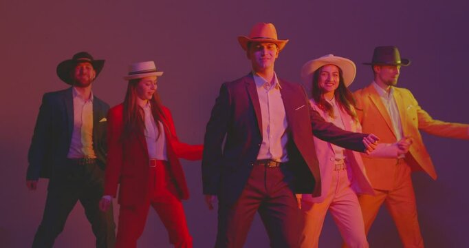 Young dance team in colorful costumes and hats dance together. The disco music sets the mood for a lively party, dancers enjoy the crazy atmosphere, illuminated by neon lights, and the sound of music.