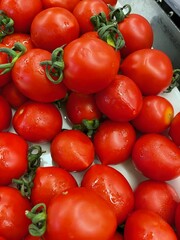 A close-up of fresh, ripe red tomatoes with green stems, showcasing their vibrant color and natural texture at a market.
