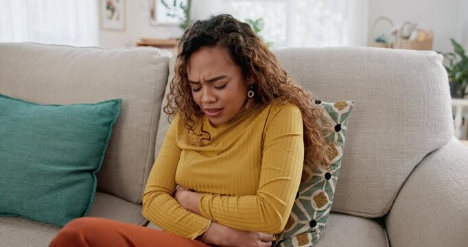 Woman, stress and stomach ache on sofa with PMS, period cramps and rubbing for relief. Menstruation, female person and hands on abdomen with constipation issue, gut health or anxiety in home for pain
