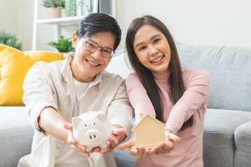 Happy asian family young couple love hand holding piggy bank to save and model house for saving...