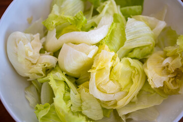 A very delicious-looking fresh salad made from iceberg lettuce is served in a white bowl. It looks very healthy, refreshing, and fresh.