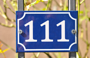 A blue house number plaque, showing the number hundred and eleven (111) 