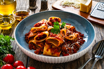 Paccheri con ragù alla bolognese - noodles with bolognese sauce and grated parmesan cheese served in bowl on wooden table
