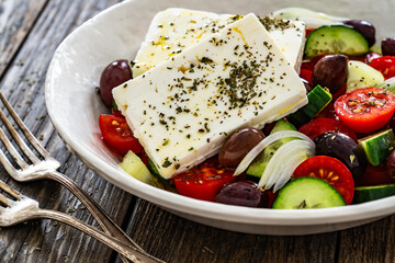 Greek style salad - fresh vegetables with feta cheese, pita bread and black olives served in bowl on wooden table
