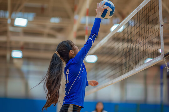 Girl in a blue shirt is about to hit a volleyball. The girl is wearing a ponytail and is reaching for the ball