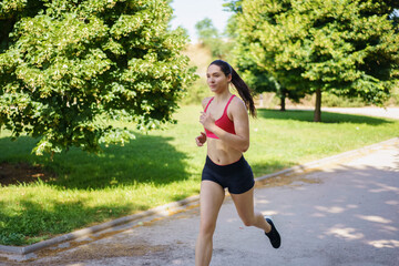 A young woman is jogging in the park on a sunny day, enjoying her workout in the fresh air surrounded by nature