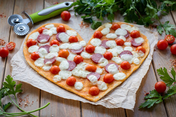 Pizza in the shape of a heart. Pizza with salami, tomatoes, mozzarella and tomato sauce on a wooden table.