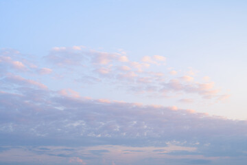 Bright blue sky with clouds lit by early morning sunshine. Blue, white, purple, and orange. Nice sky background