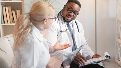 Doctors cooperation. Medical discussion. Professional smart man physician checking diagnosis report with x ray scan together with woman practitioner on couch at hospital.