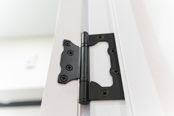 This image features a detailed closeup of a black door hinge that is affixed to a crisp white door,...