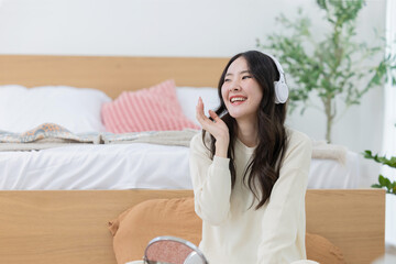 Asian woman listening music trough her wireless headphones in her bedroom