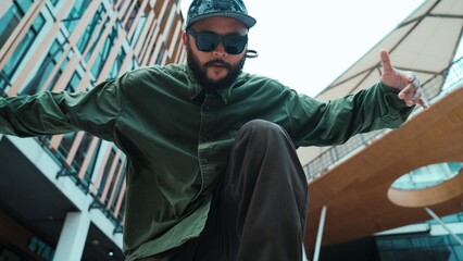 Low angle view of hipster pose in hip hop style surrounded by mall view. Portrait of sporty asian hip hop choreographer dancing break dance while looking at camera. Outdoor sport 2024. Hiphop.