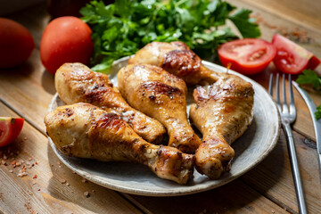 Hearty lunch: grilled chicken legs on a white plate on a wooden table. Close-up