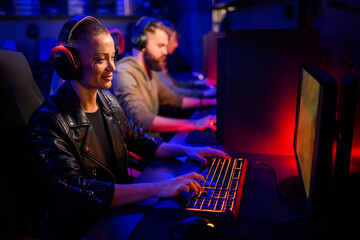 Gamer girl with headset playing video game on pc in internet cafe.