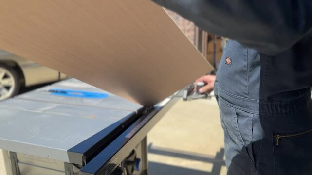 A woodworking expert cuts plywood on a table saw in a residential garage in the afternoon