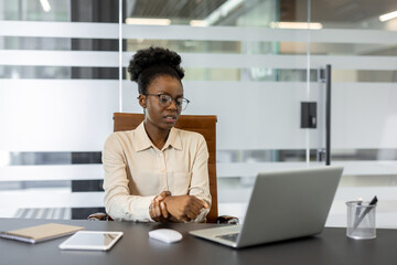 Focused African American businesswoman seated at desk in contemporary office holding wrist in pain....