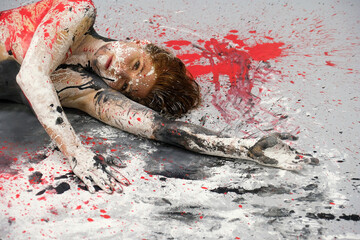 sexy nude redhead woman covered in black, white, and red paint lies on the floor, surrounded by...