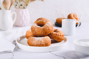 Delicious donuts in powdered sugar on a plate on a white table