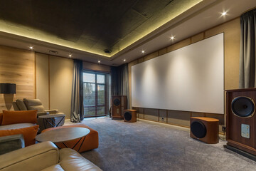 Modern interior of a home theater. Comfortable leather chairs, a large screen with speakers on both sides. Window with blackout curtains.
