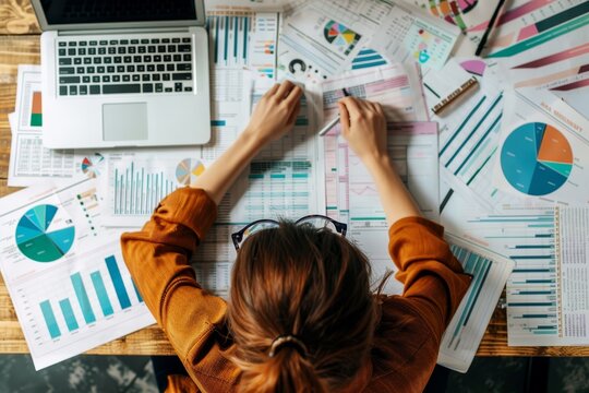 A person is focused on reviewing various data reports surrounded by colorful charts and graphs, working diligently at a wooden table during the day.