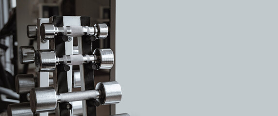 Dumbbell Rack in Fitness Gym close-up. Set of steel dumbbells of different weight. Business card with copy space on gray background. Sporting equipment for strong muscles. Sport shop. Club membership