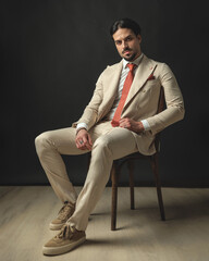 sexy and masculine man in beige suit sitting on chair