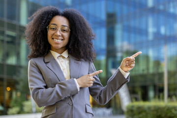 Confident African American business woman in formal attire pointing with both hands, smiling warmly...