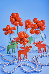bright New Year composition with festive toy deer, toy viburnum in glass bottles and silver long garland of small beads on blue background close-up, Seasons greeting card template