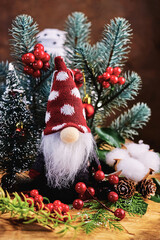Obraz premium kind cute little gnome in a red hat with white polka dots with a long beard against the background of a Christmas tree, branches and Christmas decor, New Year celebration, holiday card