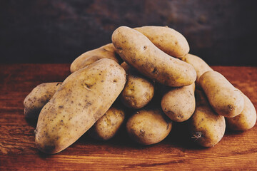 still life of large potato tubers laid out in a pile on a wooden table, dark background, close-up