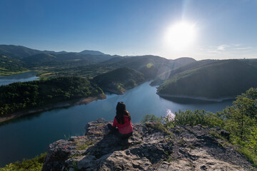 A Woman Sitting On A Rock Looking Out Over A Beautiful Nature. A Beautiful View Of A Lake And Mountains. rare view