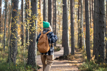 Interested woman tourist with backpack enjoy stroll on eco forest path in cold fall day. Female wearing warm clothes walks in woods park, breathing cool fall air observing changes in nature, rear view
