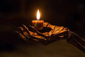 Skeleton hand holding a burning candle in a dark room
