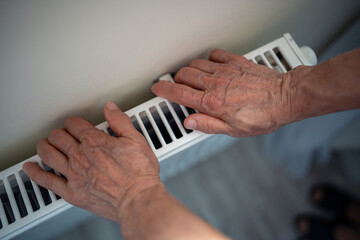 Woman hands resting on heating radiator, checking warmth. Female struggling in winter, energy...