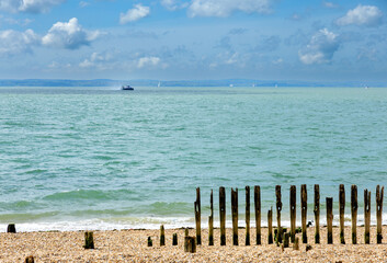 The strand of Portsmith, turquoise beach with wooden breakwaters in the foreground and a hoovercraft and some sailboats in the background.