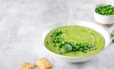 Green pea cream soup with crackers on a gray table. Top view.