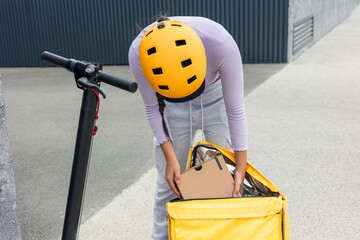 unrecognized Latin courier with yellow helmet taking package from backpack for home delivery