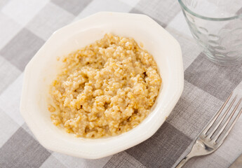 There is portion of freshly prepared milk oatmeal porridge in plate. Traditional dietary European breakfast.