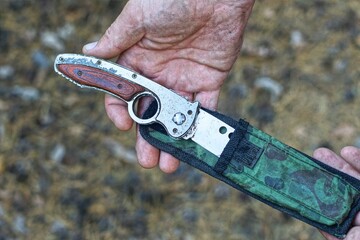 aggressive man takes out a sharp dangerous iron knife with a brown handle gray army dirty modern...