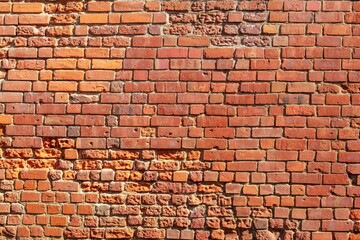 This image shows a close-up of a weathered red brick wall, highlighting its rough texture. The...