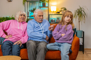 Angry grandfather and grandmother scolding granddaughter for bad behavior and disobedience on sofa,...