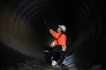 A female construction engineer with a reflective safety jacket inspects inside the huge tube,...