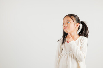 Portrait Asian kid girl deep in thought, standing with chin in hand, pondering a question. Studio...