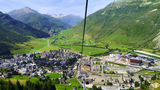 Travel in Overhead Cable Car with Panoramic View on the Swiss Alps and Valley and Cityscape and Golf Course in a Sunny Summer Day in Andermatt, Uri, Switzerland, Europe
