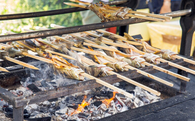 Traditional Japanese outdoor cooking, grilling fish on skewers over open fire, charcoal grilling concept