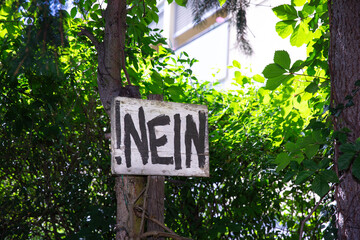 Wooden sign with bold black letters, Nein, hanging on a tree in a green forest, caution, negativity concept