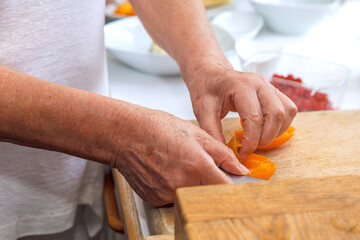 Hands carefully chopping orange bell pepper on wooden cutting board in kitchen, cooking preparation concept