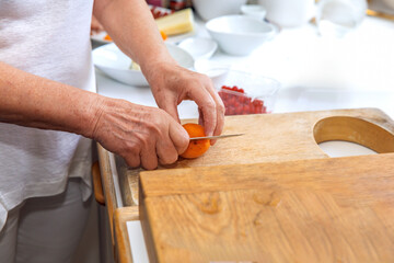 Hands slicing orange apricot on wooden cutting board in kitchen, cooking preparation concept